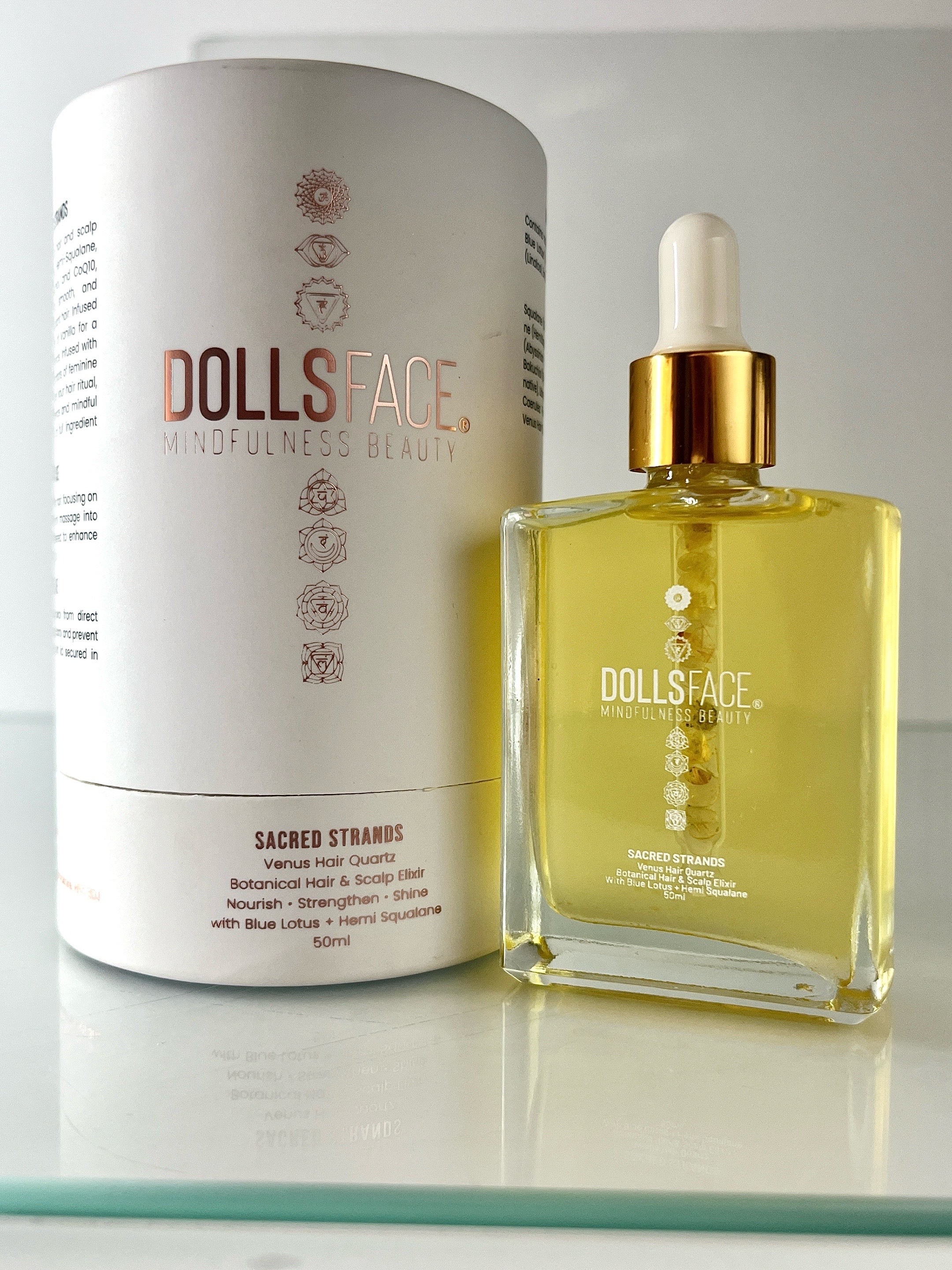 Sacred Strands 50 ML glass bottle with Venus Hair Quartz crystal in pipette, featuring luxurious Blue Lotus and Hemi-Squalane oil, displayed next to white soft-touch cylinder packaging with rose gold print