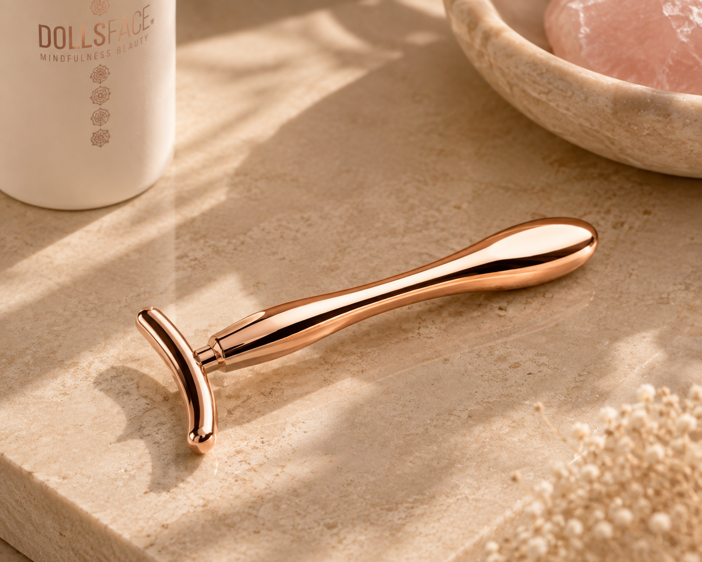 DOLLSFACE® rose gold T shaped Ritual Bar for facial massage on a warm stone surface.